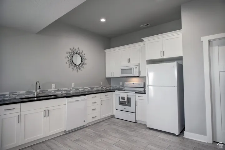 Kitchen featuring white appliances, dark countertops, a sink, white cabinetry, and visible vents