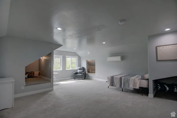 Carpeted bedroom featuring lofted ceiling, a wall mounted air conditioner, recessed lighting, and baseboards