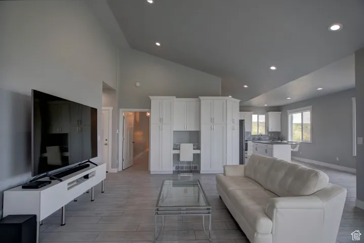 Living room with light wood-type flooring, recessed lighting, high vaulted ceiling, and baseboards