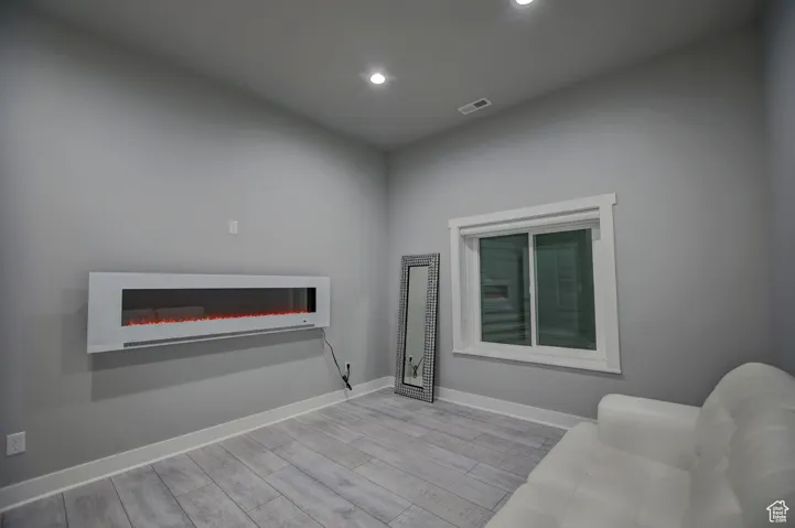 Living room featuring visible vents, baseboards, a glass covered fireplace, recessed lighting, and wood finished floors