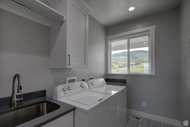 Clothes washing area featuring a sink, cabinet space, separate washer and dryer, visible vents, and baseboards