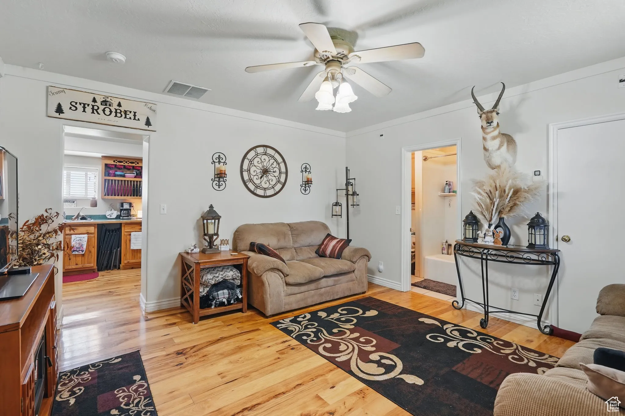 Living area featuring wood finished floors, visible vents, ceiling fan, and crown molding