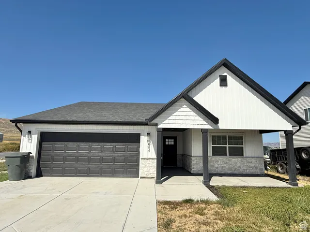 View of front of property with an attached garage, stone siding, a porch, driveway, and a shingled roof