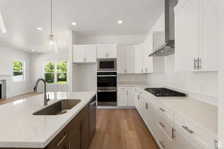 Kitchen with light wood finished floors, white cabinetry, wall chimney exhaust hood, appliances with stainless steel finishes, and recessed lighting