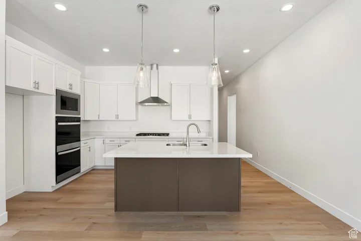 Kitchen with light wood-type flooring, white cabinetry, light countertops, recessed lighting, and a center island with sink