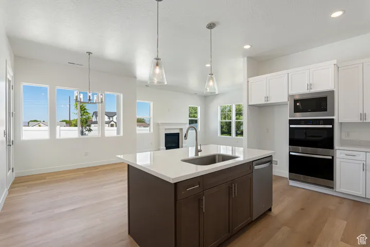 Kitchen with light wood finished floors, appliances with stainless steel finishes, a textured ceiling, white cabinets, and recessed lighting