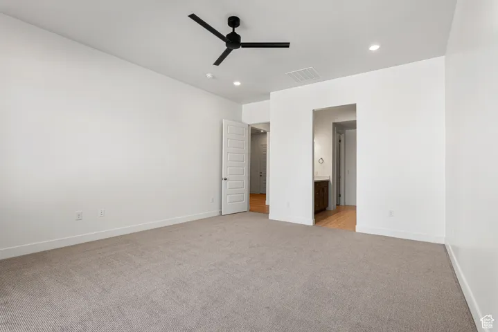 Unfurnished bedroom featuring light colored carpet, recessed lighting, ensuite bathroom, and a ceiling fan