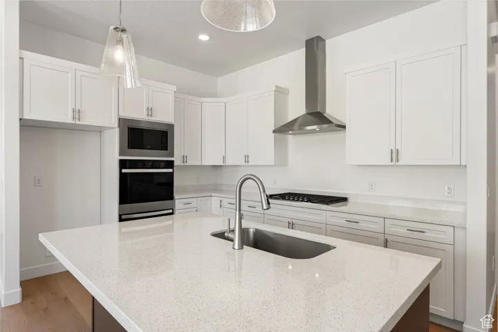 Kitchen featuring wall chimney range hood, stainless steel appliances, wood finished floors, white cabinetry, and light stone counters
