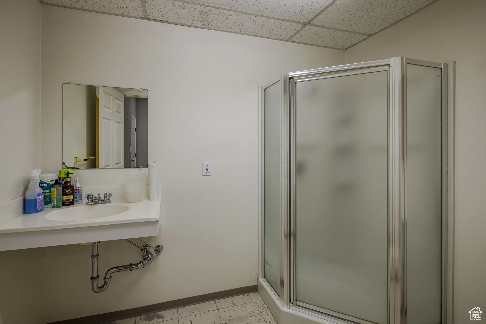 Bathroom featuring a shower stall, baseboards, a sink, and a drop ceiling