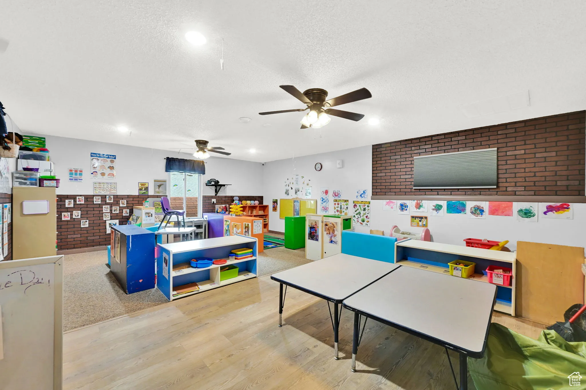 Rec room with wood finished floors, ceiling fan, brick wall, and a textured ceiling