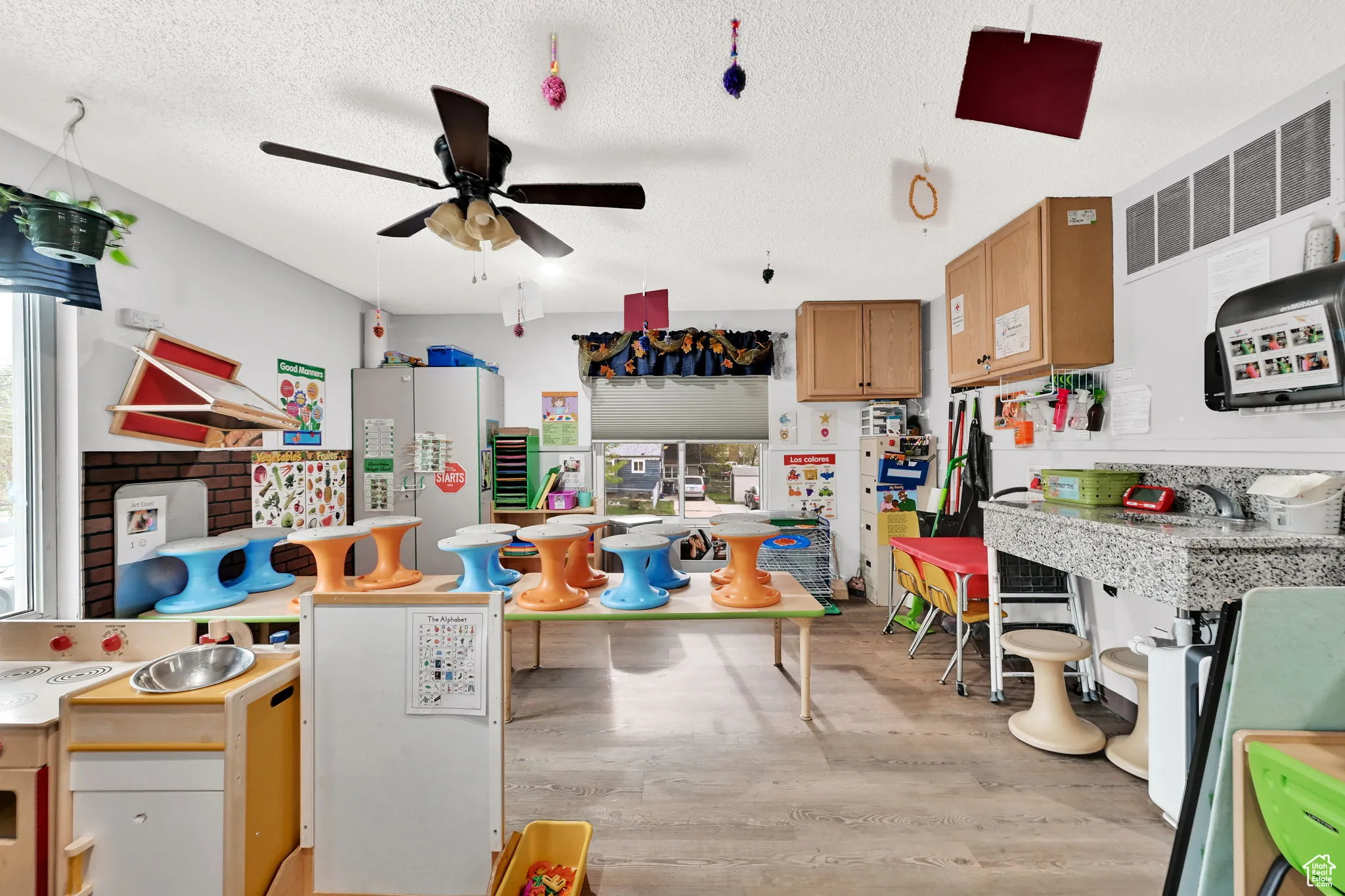 Kitchen with a textured ceiling, ceiling fan, freestanding refrigerator, light wood-type flooring, and brown cabinetry