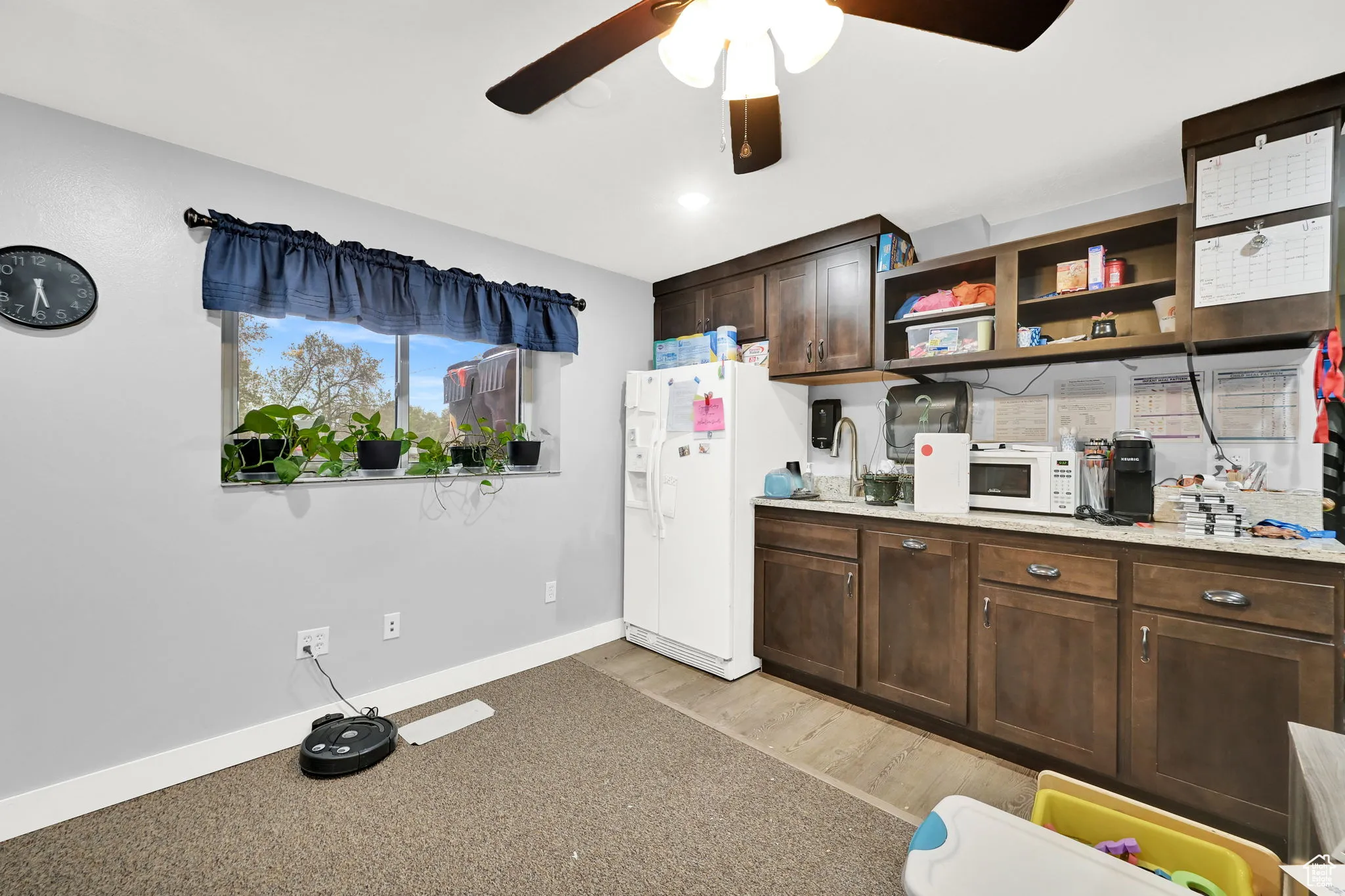 Kitchen with light wood finished floors, open shelves, a ceiling fan, white appliances, and dark brown cabinets