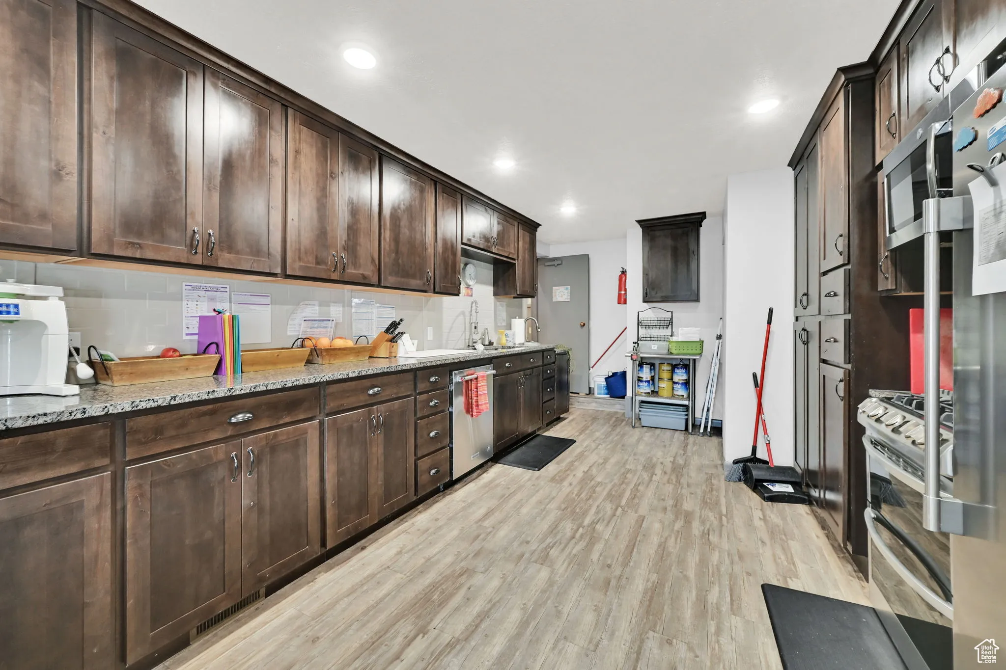 Kitchen featuring light wood-style flooring, appliances with stainless steel finishes, dark brown cabinets, light stone countertops, and recessed lighting