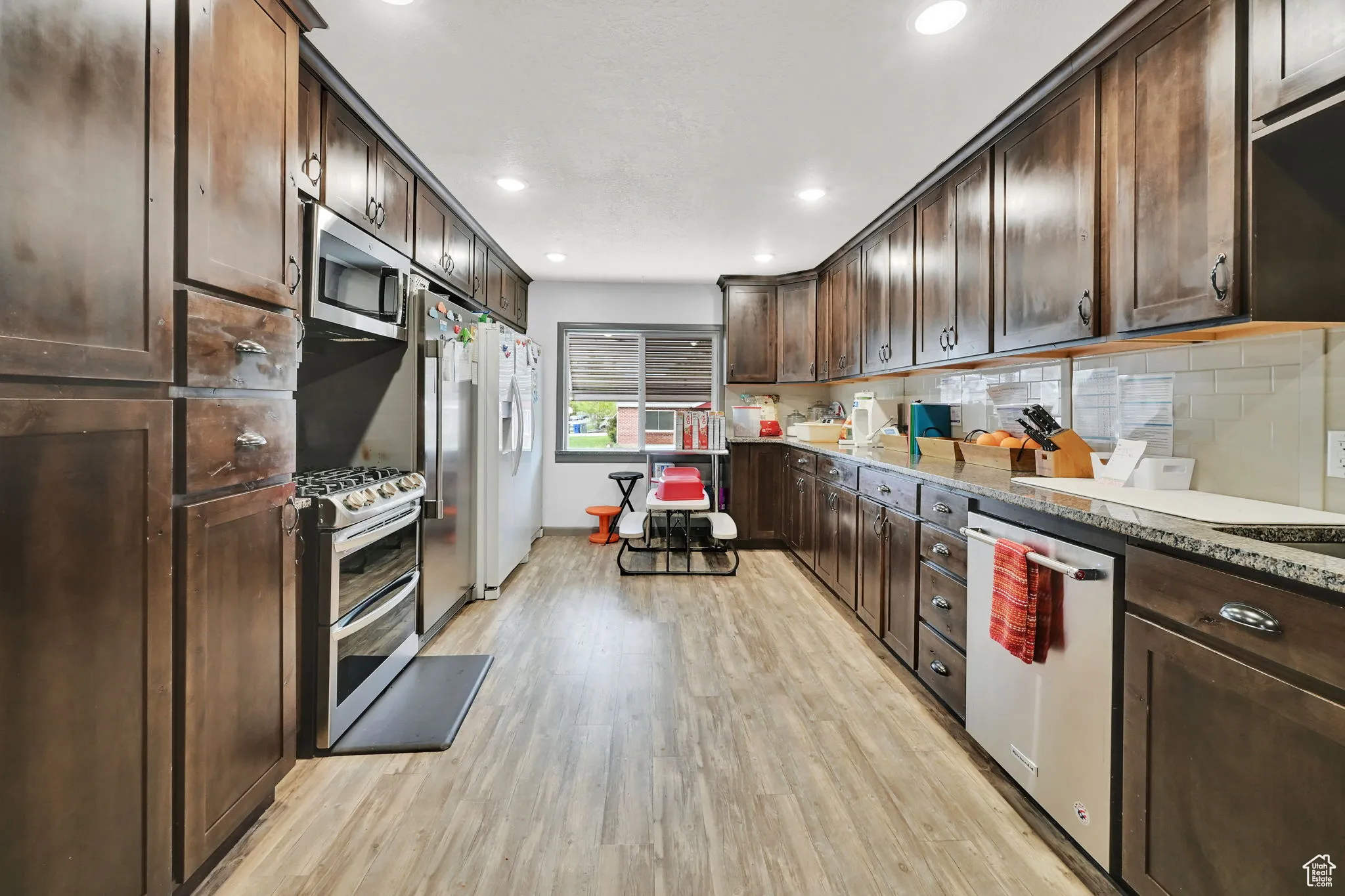Kitchen with tasteful backsplash, recessed lighting, stainless steel appliances, dark brown cabinets, and light wood-type flooring