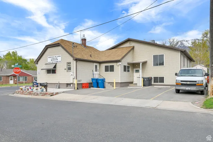 View of front of house with roof with shingles, a chimney, and uncovered parking