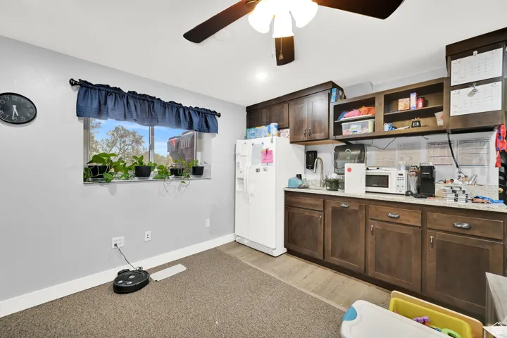 Kitchen with light wood finished floors, open shelves, a ceiling fan, white appliances, and dark brown cabinets
