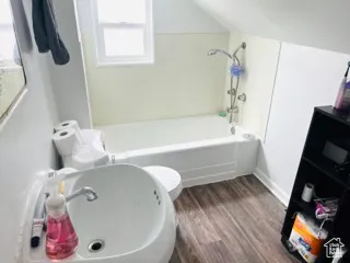 Full bathroom featuring a sink, baseboards, wood finished floors, and plenty of natural light