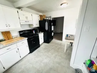 Kitchen featuring beamed ceiling, under cabinet range hood, light countertops, white cabinets, and black appliances