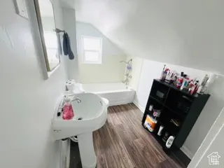 Bathroom featuring a tub to relax in, lofted ceiling, and wood finished floors
