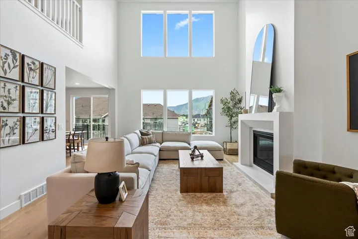 Living room featuring a high ceiling, a glass covered fireplace, baseboards, wood finished floors, and visible vents