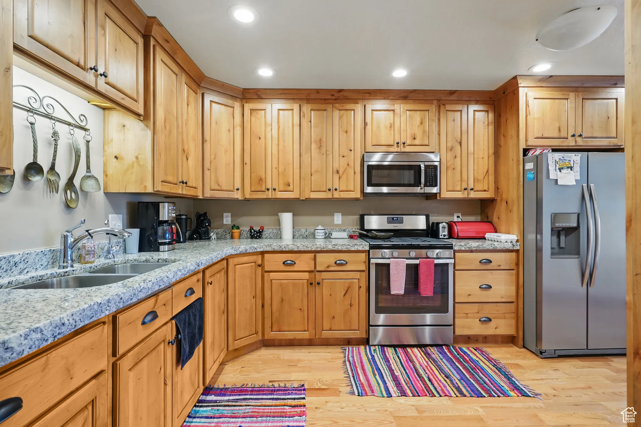Kitchen with stainless steel appliances, light stone countertops, a sink, and light wood-type flooring