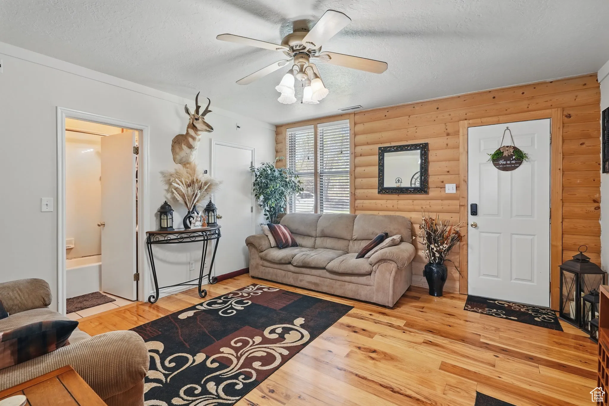 Living area with visible vents, log walls, a textured ceiling, a ceiling fan, and light wood-style flooring