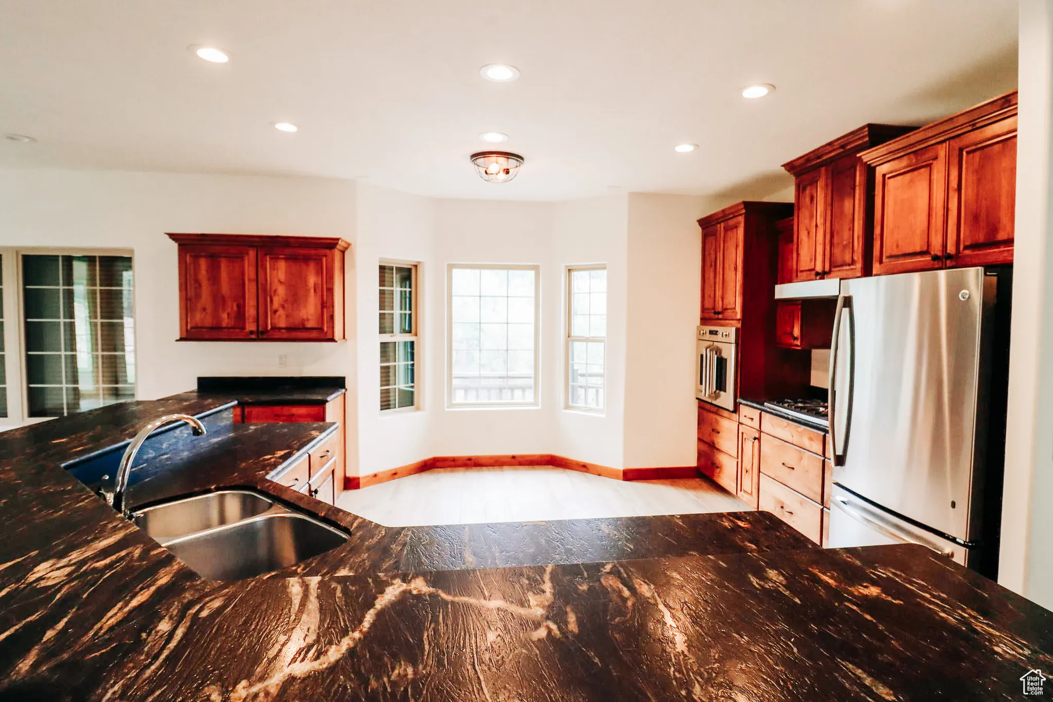 Kitchen featuring freestanding refrigerator, dark stone countertops, recessed lighting, wall oven, and reddish brown cabinets
