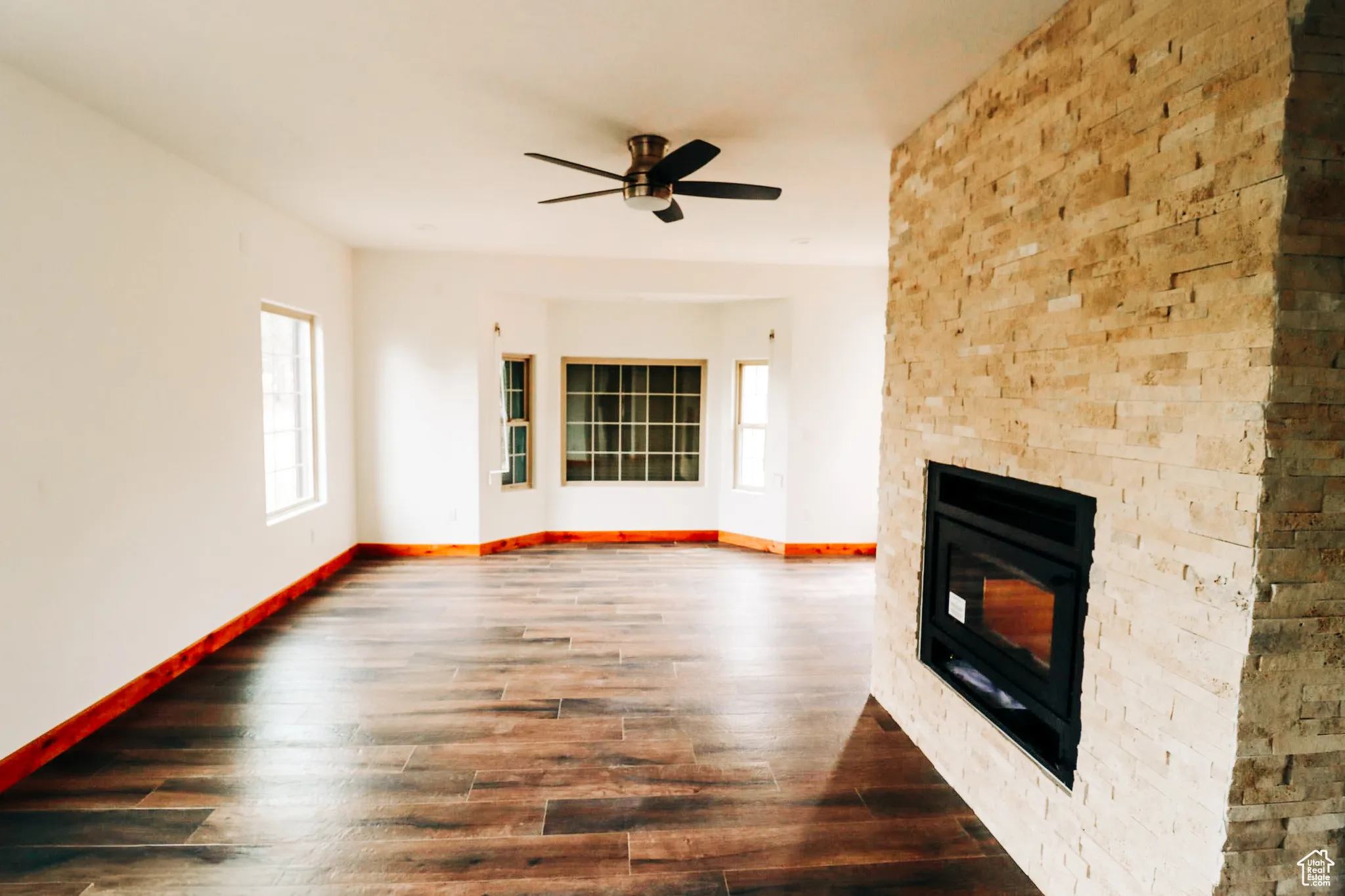 Unfurnished living room with a fireplace, dark wood-style floors, and ceiling fan
