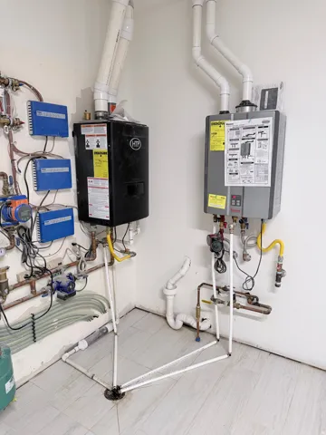 Utility room featuring two wall-mounted tankless water heaters, extensive plumbing infrastructure, and a light-toned tile floor