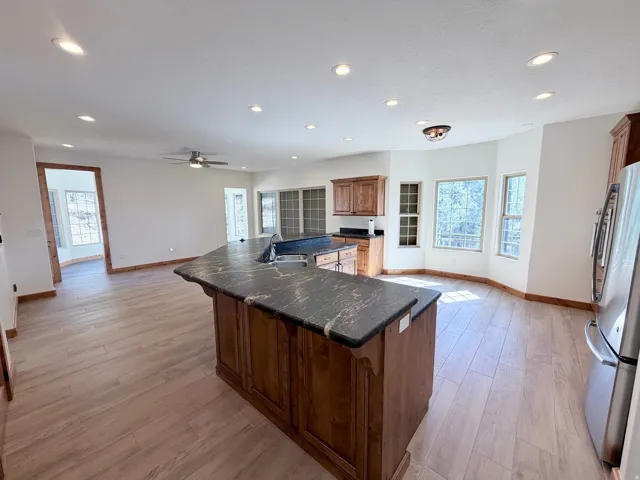 Open concept kitchen featuring a large central island with a dark countertop and integrated sink, recessed lighting, wood-finish flooring, and ample natural light from multiple windows