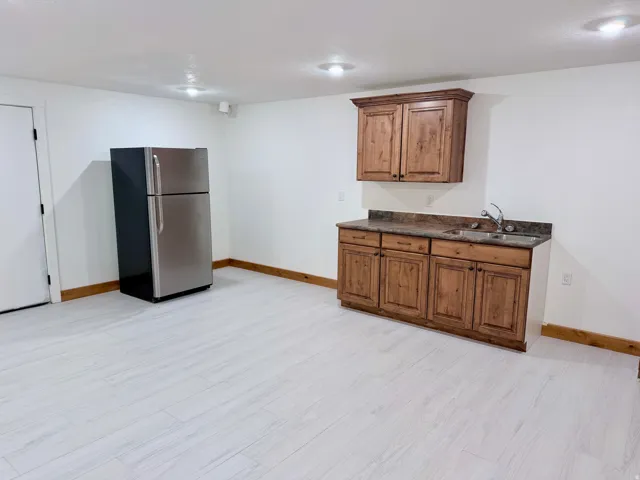 Kitchenette featuring wood-finish cabinetry, a sink with a chrome faucet, and a stone-finish countertop