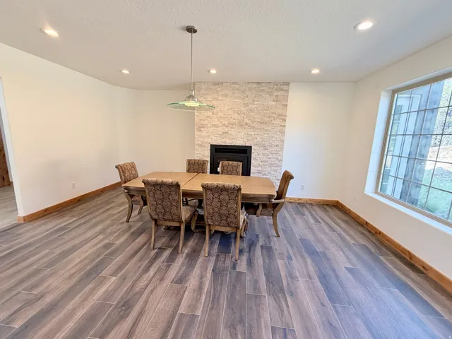 Spacious room featuring wood-finish tile flooring, a fireplace with a stacked stone facade, and a large window providing ample natural light
