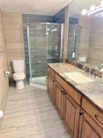 Bathroom featuring a glass-enclosed shower, a wood-finish vanity with an integrated sink, a dark stone-look countertop, and a large wall mirror