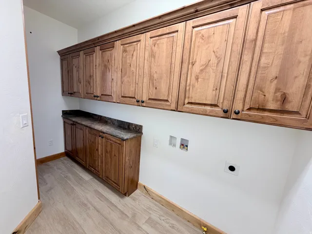Laundry area featuring extensive wood cabinetry with dark hardware, a countertop with a stone-look finish, and light wood-finish flooring
