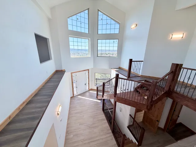 Vaulted ceilings with high windows, light wood-finish flooring, and a multi-level wooden staircase with wrought iron balusters