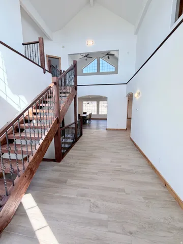 Vaulted entry featuring a grand staircase with wood treads and wrought iron spindles, wood-finish flooring, and a second-story arched window with ceiling fans