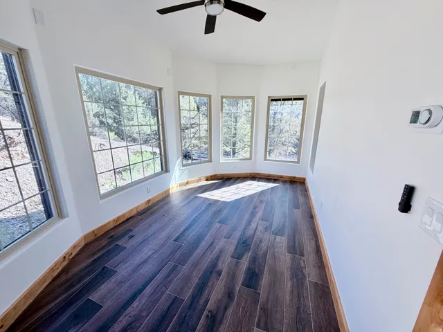 Sun-filled room featuring five large gridded windows, dark wood-finish flooring, natural wood baseboards, and a ceiling fan