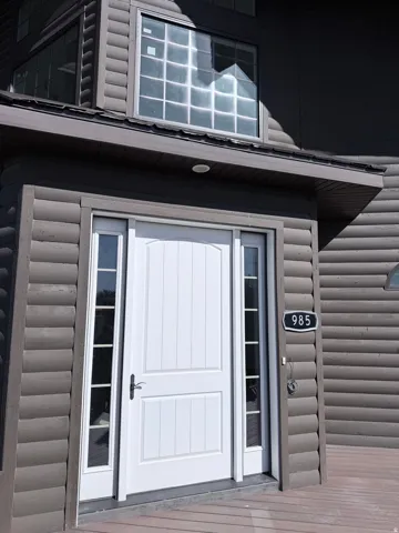 White paneled entry door with sidelight windows, complemented by a wood-finish exterior featuring horizontal log-style siding