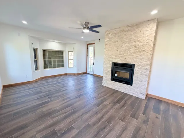 Expansive living space featuring wood-finish tile flooring, a stacked stone fireplace, a bay window with multiple panes, recessed lighting, and a ceiling fan