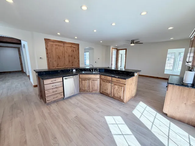 Spacious kitchen island featuring dark countertops, a stainless steel dishwasher, and a double basin sink