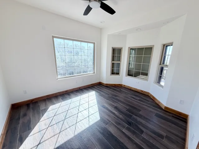 Room featuring dark wood-finish flooring, white walls, and a ceiling fan