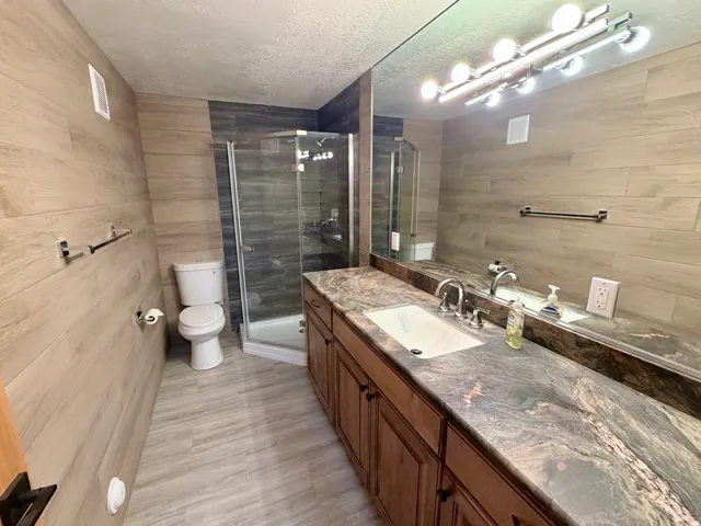 Spacious bathroom featuring a frameless glass shower, a wide vanity with an integrated sink, a large wall mirror, and wood-look tile flooring