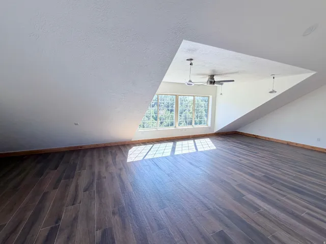 Spacious room featuring wood-finish flooring, a multi-pane window, a ceiling fan, and sloped ceilings
