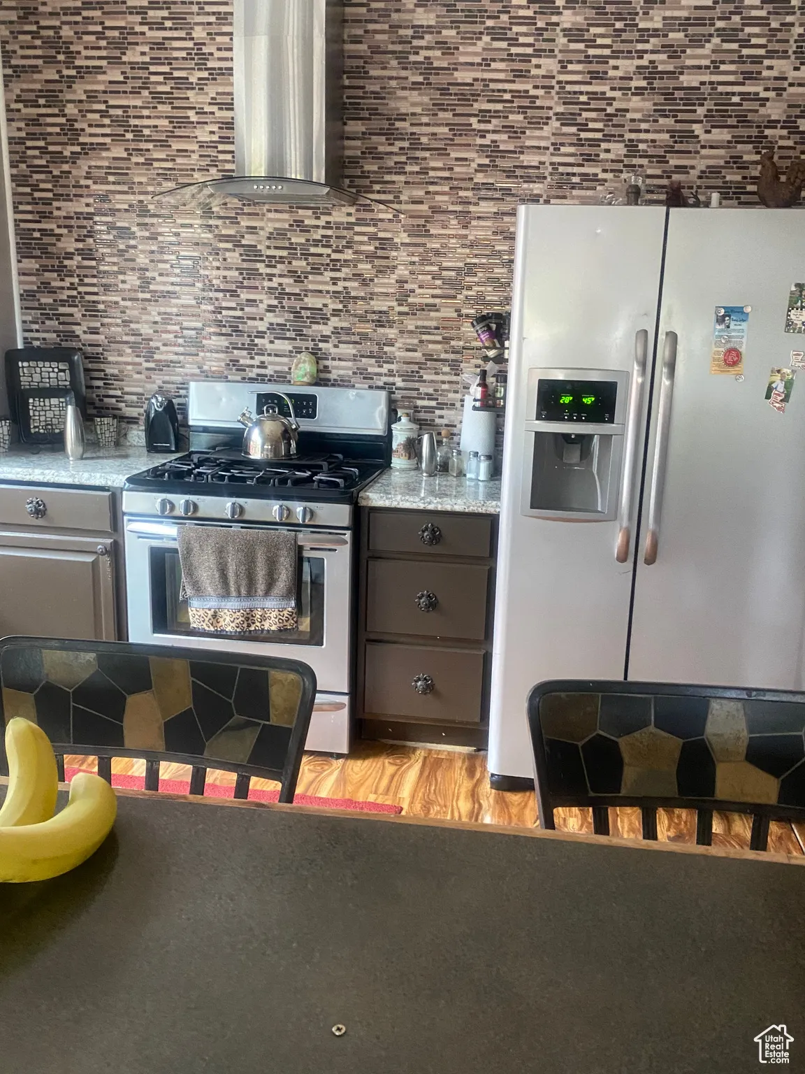 Kitchen featuring wall chimney exhaust hood, backsplash, light wood-style floors, appliances with stainless steel finishes, and gray cabinets