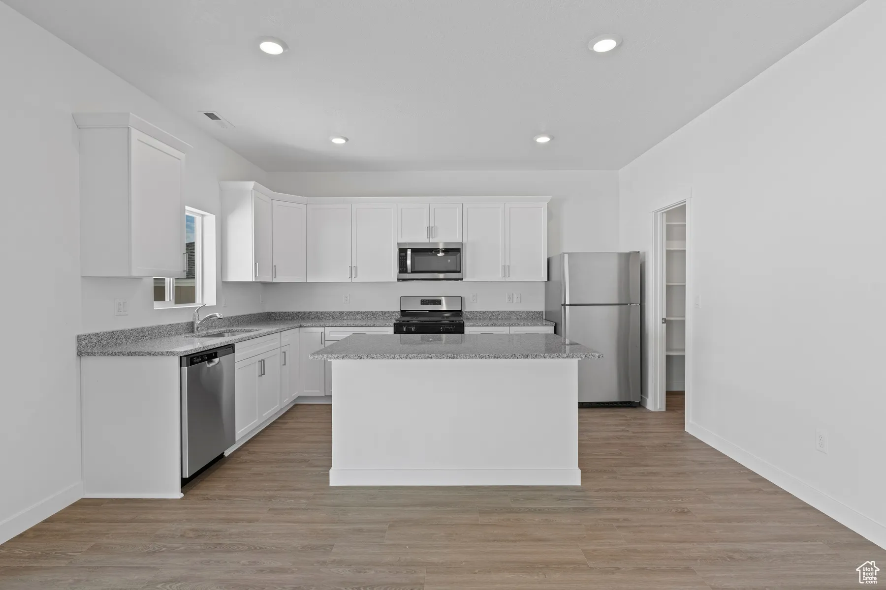 Kitchen featuring a sink, stainless steel appliances, a kitchen island, and white cabinets
