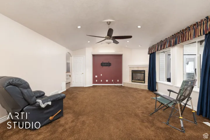 Unfurnished room with vaulted ceiling, dark colored carpet, a tile fireplace, arched walkways, and a ceiling fan