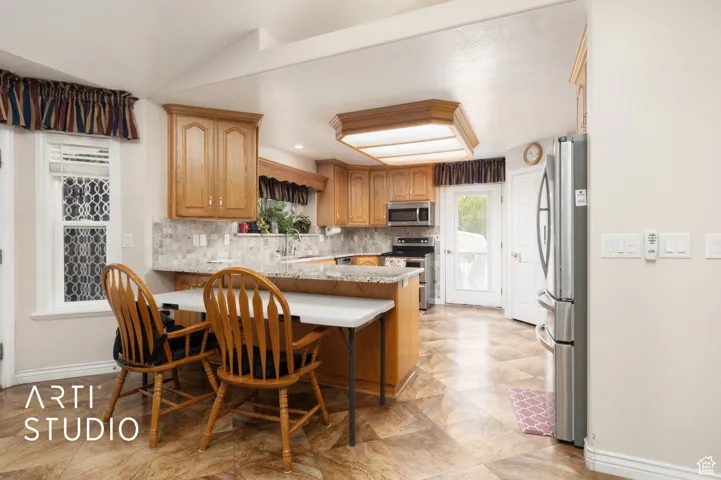 Kitchen featuring backsplash, a peninsula, appliances with stainless steel finishes, a breakfast bar, and light stone counters