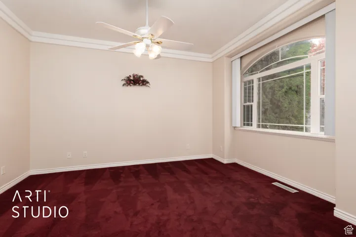 Empty room with dark colored carpet, a ceiling fan, and ornamental molding