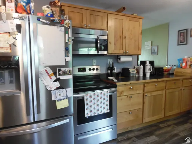 Kitchen with appliances with stainless steel finishes, dark wood-style floors, dark countertops, and light brown cabinetry