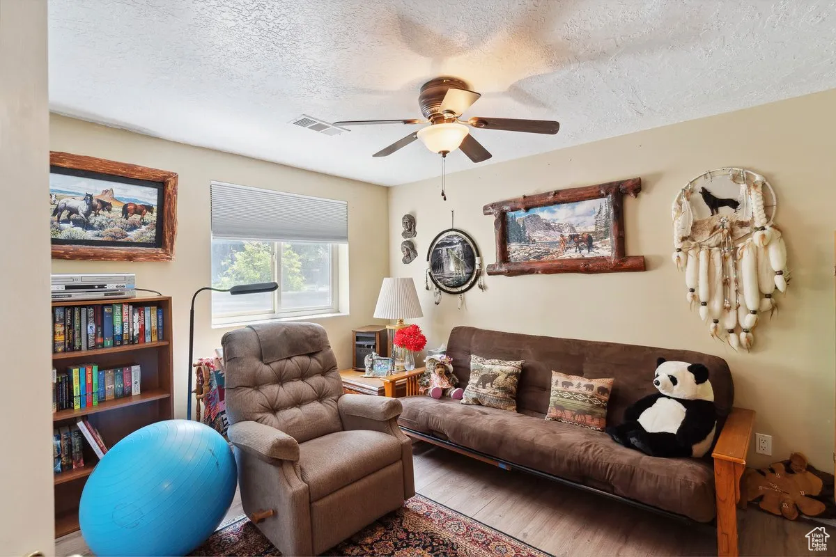 Living area featuring a ceiling fan, wood finished floors, and a textured ceiling